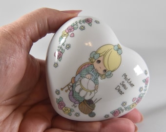 Puede incluir: Caja de porcelana blanca en forma de corazón con una ilustración colorida de una niña cosiendo. La caja tiene un diseño floral y el texto "Mother Sew Dear" en el lateral.