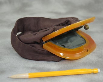 May include: A brown fabric purse with a yellow plastic clasp. The purse is open and the inside is lined with a gray fabric.