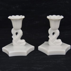 May include: Pair of white milk glass candle holders with a fish design. Each holder has a scalloped top and a hexagonal base.