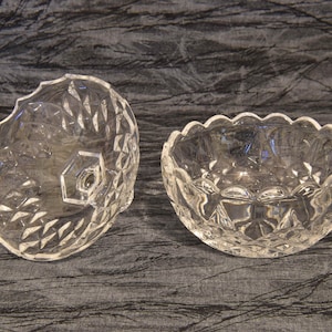 May include: Two clear, cut-glass bowls. One bowl is round with a scalloped edge, and the other is a lid with a hexagonal knob. Both have a diamond pattern. The bowls are likely for serving or display.