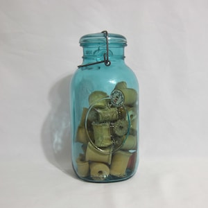 Frasco ideal de bolas de dos cuartos con águila, fianza y tapa y 27 carretes en el interior. Tarro ideal Aqua A8 Ball con asa de alambre y tapa de vidrio.
