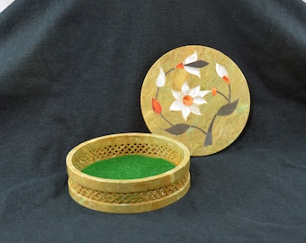 May include: A round, green, felt-lined, stone trinket box with a carved lattice design. The lid is made of stone and features a floral design with white and red flowers.