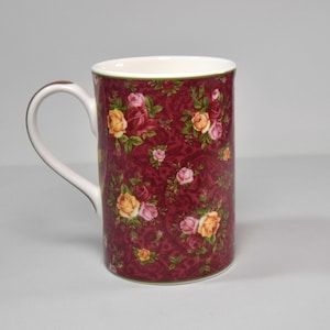 May include: A red ceramic mug with a floral pattern featuring pink and yellow roses. The mug has a white interior and a white handle.