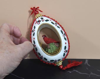 Adorno navideño vintage de huevo de cardenal rojo en forma de diorama. Adorno de huevo de plástico blanco con un pájaro rojo en su interior y un rick rack rojo. Decoración navideña.