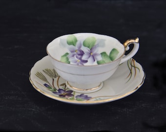Taza de té vintage Lefton con platillo a juego, decorada con violetas y detalles dorados. Taza de té y platillo de porcelana fina, ambos fabricados en Japón.