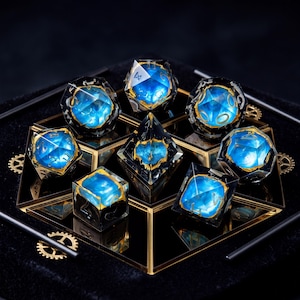 Op de afbeelding: Een set van zeven veelzijdige dobbelstenen met een heldere buitenkant, een levendige blauwe kern en goudkleurige accenten. De dobbelstenen hebben gegraveerde cijfers en zijn gerangschikt op een reflecterend zwart oppervlak met gouden tandwielen.