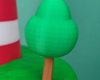 Puede incluir: Una escena en miniatura impresa en 3D con un árbol verde con un tronco marrón sobre una base verde, junto a un faro a rayas rojas y blancas. El fondo es de color turquesa sólido.
