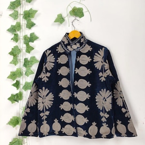 May include: A navy blue jacket with beige floral embroidery. The jacket has a high collar and a striped lining. It is hanging on a wooden hanger against a white background, with green ivy accents.