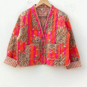 Könnte beinhalten: Gesteppte Jacke mit Tigerprint. Die Jacke hat einen V-Ausschnitt, zwei Taschen und Holzknöpfe. Das Design integriert vertikale Streifen in Orange- und Rosatönen mit Tigerillustrationen.