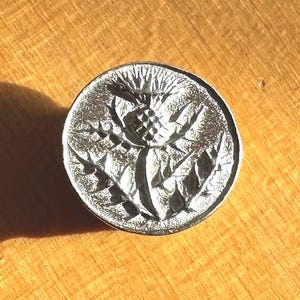 Thistle button, a 1/2-inch round pewter button designed and engraved by Randy Miller