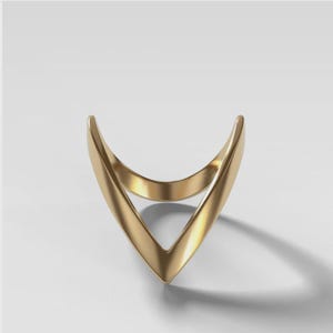 Puede incluir: Un anillo dorado con un diseño en forma de V. El anillo tiene una superficie lisa y pulida y una estética minimalista. El diseño abierto del anillo crea un aspecto único y moderno. El anillo es probablemente de metal.