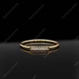 Op de afbeelding: Een gouden ring met een rechthoekige balk bezet met kleine, heldere edelstenen. De ring staat tegen een zwarte achtergrond, waardoor het ontwerp wordt benadrukt. The Precious Jewelz staat boven en onder in de afbeelding.