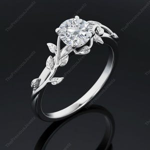 Op de afbeelding: Een zilveren ring met een grote, ronde, heldere edelsteen. De ring heeft een bladeren ontwerp op de band en rond de edelsteen setting. The Precious Jewelz is op de afbeelding afgedrukt.