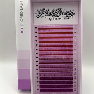 Könnte beinhalten: Eine Schachtel mit farbigen Nerzwimpern in Rot- und Lilatönen. Die hellviolette Schachtel trägt den Schriftzug "Plush Beauty by YULMA" und "PREMIUM MINK LASHES". Die Wimpern sind in Reihen mit Längen von 10 mm bis 13 mm angeordnet.