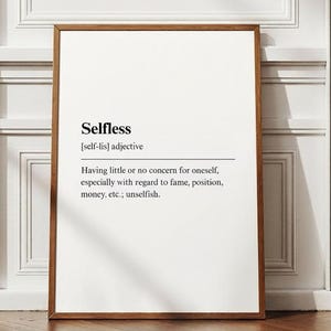 Puede incluir: Un marco con la definición de "Selfless" en texto negro sobre fondo blanco. La definición incluye la pronunciación y el significado de la palabra. El marco es marrón, contra una pared blanca y un suelo de madera.
