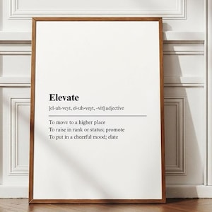 以下が含まれることがあります： 「Elevate」という言葉とその定義が書かれたフレーム付きのプリント。プリントは茶色のフレームと白い背景です。テキストには「より高い場所へ移動する」などのフレーズが含まれています。白い壁と木の床に表示されています。