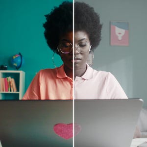 May include: A split-screen image shows a person working on a laptop. The left side is in color, featuring a pink shirt and a laptop with a heart sticker. The right side is grayscale. The background includes a shelf, a globe, and a couch.