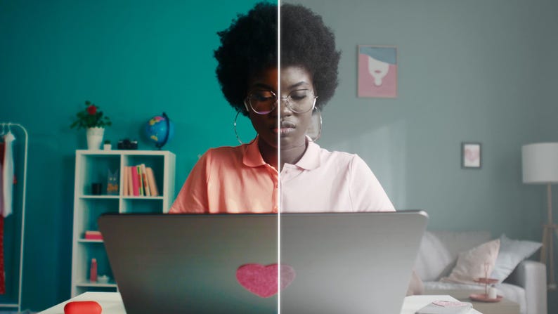 May include: A split-screen image shows a person working on a laptop. The left side is in color, featuring a pink shirt and a laptop with a heart sticker. The right side is grayscale. The background includes a shelf, a globe, and a couch.