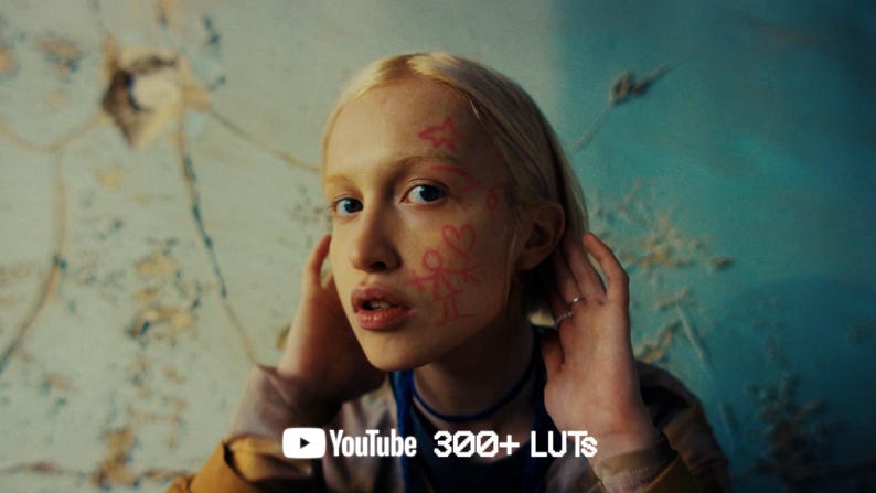 May include: A person with blonde hair and pink markings on their face, touching their head. The background is a textured wall with a YouTube logo and the text "300+ LUTs". The person is wearing a blue necklace and a gold-colored jacket.