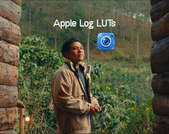 May include: A person wearing a tan jacket stands between two log walls, looking toward a forest. The text Apple Log LUTs is displayed above, accompanied by a blue camera icon. The scene is framed by dark, textured wooden logs on both sides.