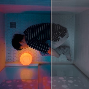 May include: A person in a striped shirt and gray pants is in a bathroom with a glowing moon-shaped lamp. The bathroom has a shower head and a light fixture. The scene is split with a color and a black and white side.