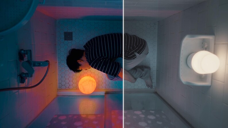 May include: A person in a striped shirt and gray pants is in a bathroom with a glowing moon-shaped lamp. The bathroom has a shower head and a light fixture. The scene is split with a color and a black and white side.