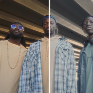 May include: Three people stand under a concrete structure. The person on the left wears sunglasses, a tan shirt, and a green jacket. The middle person wears a blue plaid shirt. The person on the right wears a denim jacket.