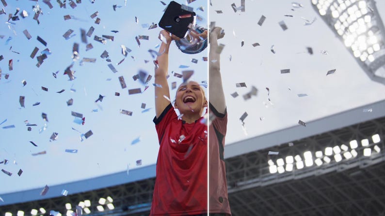 May include: A person in a red jersey celebrates a victory, holding a trophy aloft amidst falling confetti. The sky is blue, and stadium lights are visible in the background. The person is smiling and appears to be ecstatic.