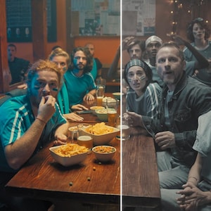 May include: A group of people in a pub, watching a sports game. They are wearing blue shirts with white stripes and have face paint. Bowls of snacks and drinks are on the wooden table. The atmosphere is lively and engaged.