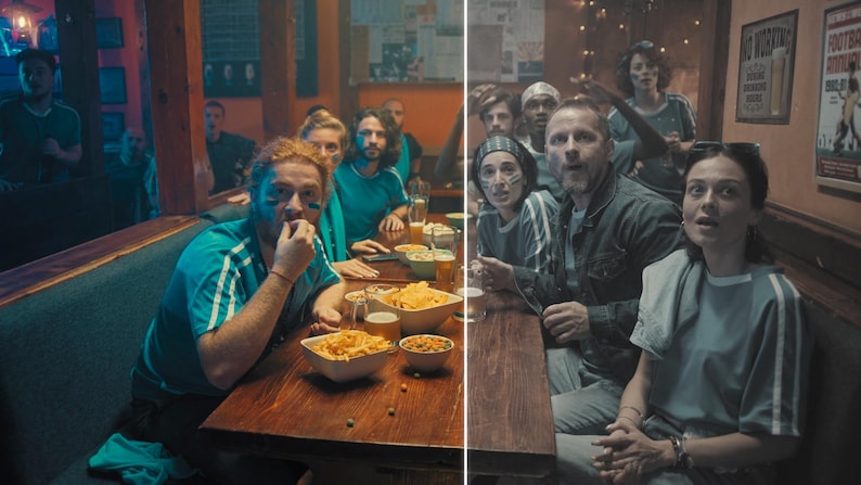 May include: A group of people in a pub, watching a sports game. They are wearing blue shirts with white stripes and have face paint. Bowls of snacks and drinks are on the wooden table. The atmosphere is lively and engaged.