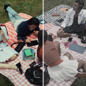 May include: A picnic scene with people on checkered blankets. One person wears a white and red soccer jersey and reads a book. Another person uses a tablet. A third person wears headphones. There are books, phones, and a black bag.