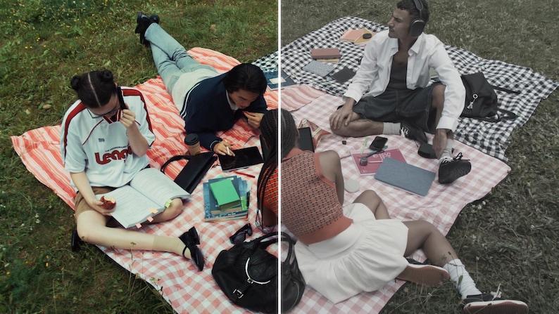 May include: A picnic scene with people on checkered blankets. One person wears a white and red soccer jersey and reads a book. Another person uses a tablet. A third person wears headphones. There are books, phones, and a black bag.