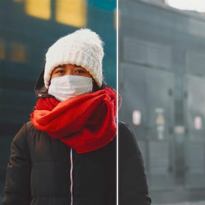 May include: A person wearing a white knit hat, a red scarf, and a black winter coat. They are also wearing a white face mask. The background is a blurred city scene.