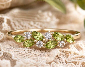 May include: A gold ring featuring a cluster of peridot and diamond gemstones. The peridot stones are a vibrant green, and the diamonds sparkle. The ring is set on a delicate, lacy surface, creating an elegant and refined aesthetic.