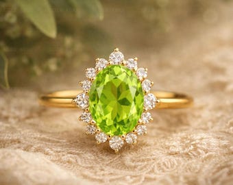 May include: A gold ring featuring a large, oval-cut, lime green peridot gemstone at the center, surrounded by a halo of small, round, clear white stones. The band is thin, polished gold, creating a bright and reflective appearance on the metal.