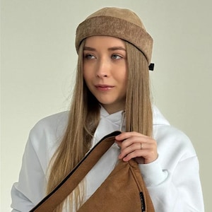 May include: A tan corduroy beanie with a wide, ribbed cuff and a smooth crown. The hat features a small black fabric tag on the side. The material has a distinct vertical texture throughout the cuff, providing a consistent look and feel.