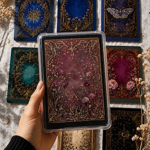 Könnte beinhalten: Eine Sammlung verzierter Tarotkarten mit aufwendigen Goldfiligran-Designs. Die Karten haben juwelfarbene Hintergründe in Blau, Grün und Burgunder, mit floralen und himmlischen Motiven. Eine Karte zeigt einen Schmetterling.
