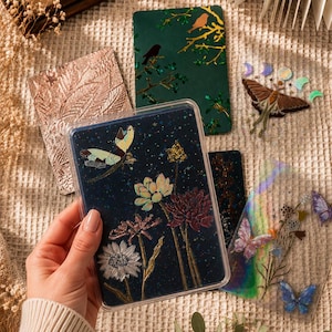 Könnte beinhalten: Eine Sammlung dekorativer Karten mit Blumen- und Schmetterlingsmotiven. Eine Karte hat einen dunkelblauen Hintergrund mit Blumen und einem Schmetterling. Andere Karten zeigen Vögel, Blätter und Schmetterlinge.