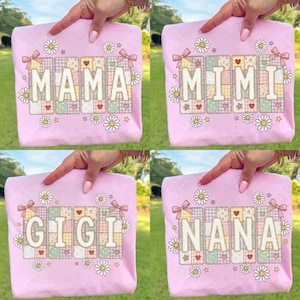May include: Pale pink sweatshirts with floral and heart details. Each top displays a different name: "MAMA", "MIMI", "GIGI", and "NANA", in a patchwork style. The names are framed by daisies and bows.