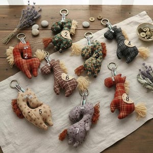 May include: A collection of handmade horse keychains in various colors and patterns. Each plush horse has a metal keyring, a fluffy mane and tail, and a number tag. The keychains are made of fabric with floral, plaid, and solid designs.