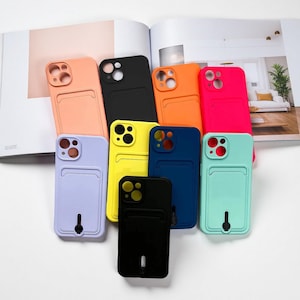 Puede incluir: Una colección de fundas de teléfono coloridas con ranuras para tarjetas. Las fundas son de varios colores, incluyendo melocotón, negro, amarillo, naranja, rosa, azul y verde menta. Las fundas están dispuestas sobre una superficie blanca con una revista abierta en el fondo.
