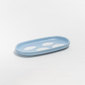 May include: A light blue ceramic tray with a cloud design. The oval-shaped tray has a light blue background with three white cloud shapes. The tray is a decorative item.