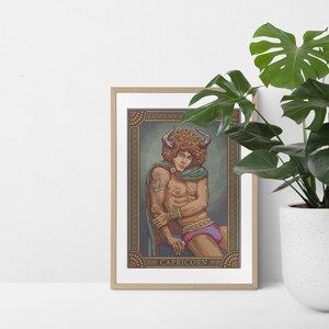 May include: Framed art print featuring a Capricorn zodiac illustration. The artwork depicts a person with curly brown hair, horns, and a green scarf. The person is wearing a bracelet and a purple and pink garment. The frame is a light brown color.
