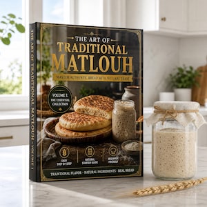 May include: A hardcover book titled The Art of Traditional Matlouh with gold lettering on a black cover, featuring images of flatbread and a glass jar of starter. Next to it sits a glass jar filled with sourdough starter and a single wheat stalk.