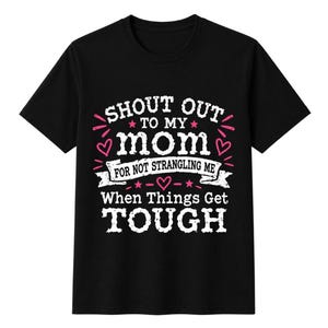 May include: A black short-sleeved t-shirt featuring white and pink text that reads SHOUT OUT TO MY mom FOR NOT STRANGLING ME When Things Get TOUGH, decorated with small pink stars and heart icons arranged around the central lettering.