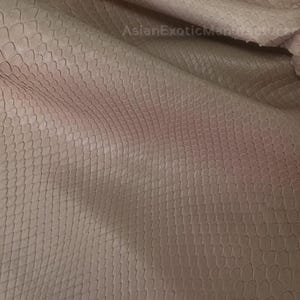 May include: Close-up of a stack of light pink snakeskin leather. The leather has a textured, scale-like pattern. The image shows the natural variations in colour and texture of the material. The leather is being held up by a hand.