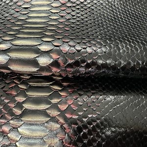 May include: Close-up of black snakeskin leather with a glossy finish. The scales are detailed and textured, with hints of red and silver. The leather has a luxurious appearance, suitable for various crafting projects.