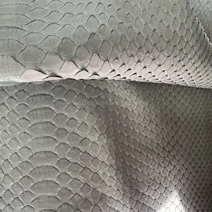 Könnte beinhalten: Nahaufnahme einer grauen Schlangenhautlederplatte. Das Leder hat ein strukturiertes, schuppiges Muster, wobei jede Schuppe leicht erhaben ist. Die Farbe ist ein gedämpftes Grau mit subtilen Farbvariationen auf der Oberfläche. Das Leder ist im Bild gefaltet.