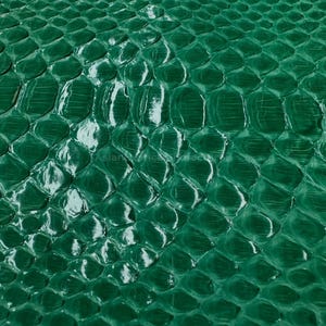 Könnte beinhalten: Nahaufnahme eines strukturierten, smaragdgrünen Schlangenmuster. Die Schuppen sind glänzend und reflektieren das Licht, wodurch Glanzlichter entstehen. Das Muster ist über die gesamte Oberfläche gleichmäßig, was auf ein durchgehendes Materialstück hindeutet. Geeignet für Hintergründe oder Designelemente.