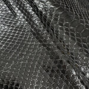 Könnte beinhalten: Nahaufnahme eines schwarzen, strukturierten Stoffes mit einem Reptilienschuppenmuster. Das Material hat eine glänzende Oberfläche, die Licht reflektiert und Glanzlichter und Schatten erzeugt. Der Stoff ist drapiert und zeigt Falten und Texturvariationen.